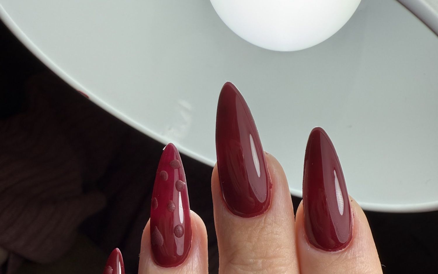 Lange bordeaux stiletto nagels met een druppelontwerp, onder de nagellamp bij Kika Nails
