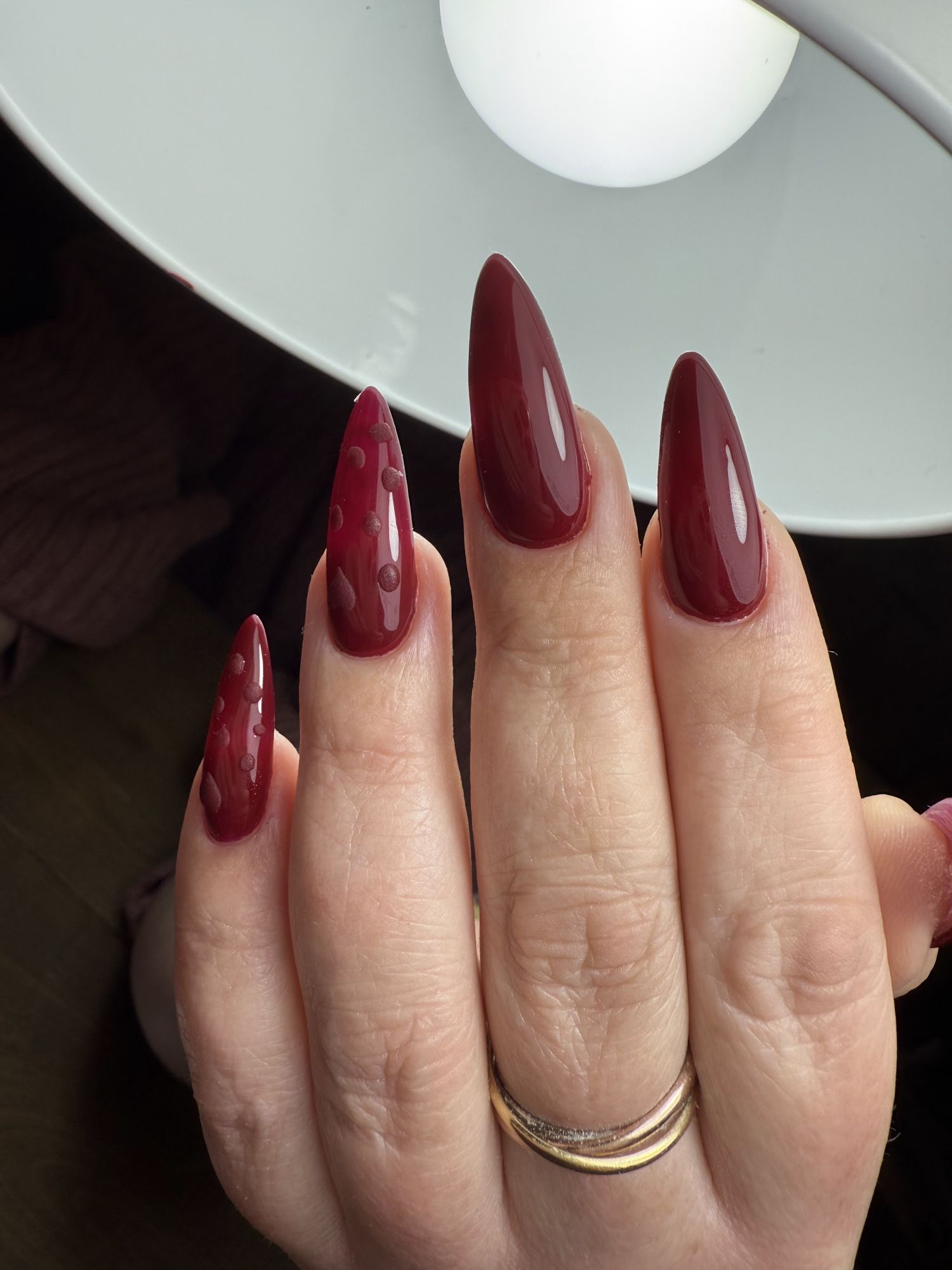 Lange bordeaux stiletto nagels, twee met een druppelontwerp, onder de nagellamp
