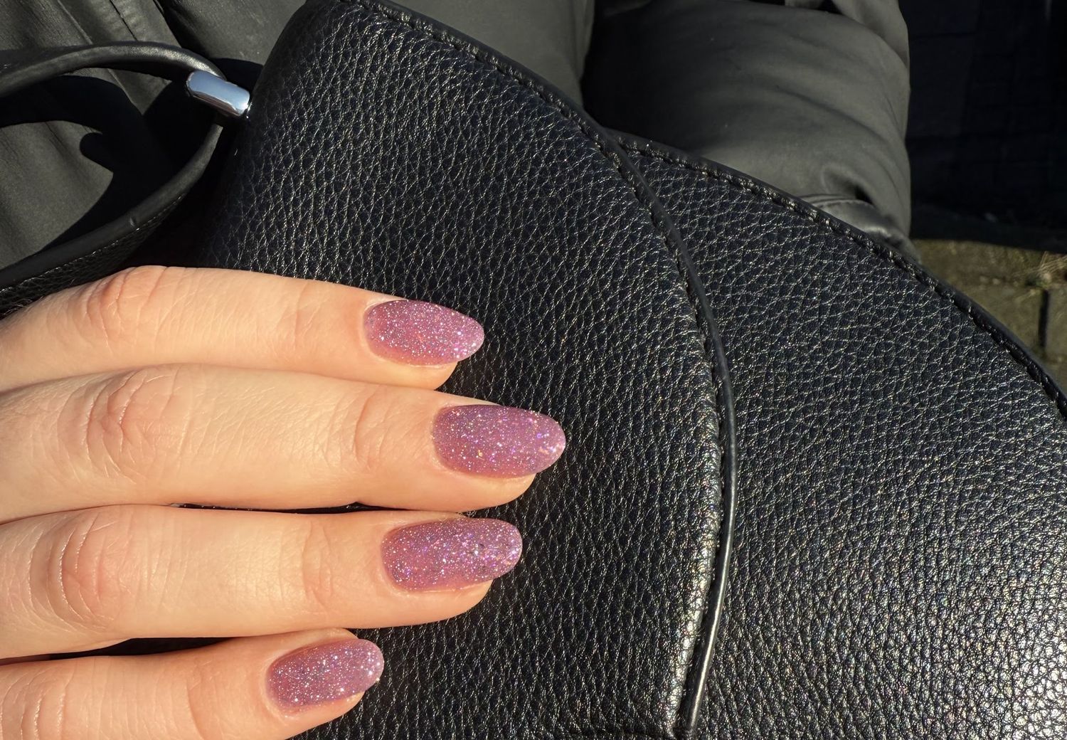 Roze glitternagels op een zwarte leren tas